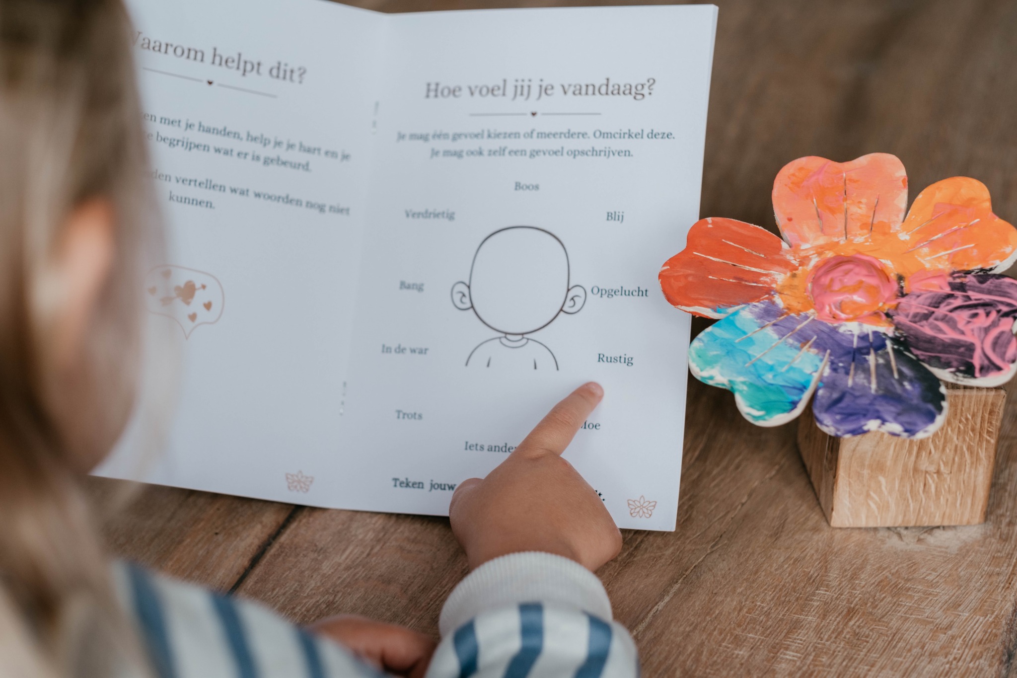 Een kind wijst een gevoel aan in het herinnerboekje, naast de beschilderde bloem